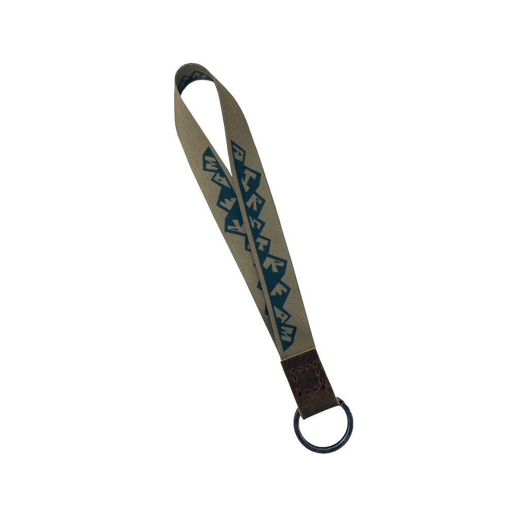 Introducing the Airstream Horizons Wristband Keychain—a stylish accessory featuring a blue geometric patterned fabric loop, secured with a brown leather connector and attached to a durable metal key ring.