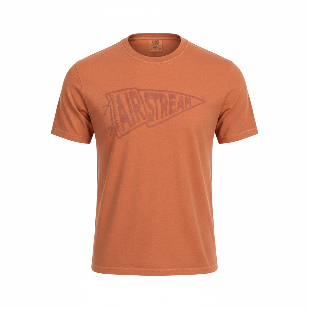 The Airstream Rally Pennant T-Shirt is a rust-colored, short-sleeve tee showcasing a vintage rally pennant graphic and the word “AIRSTREAM” across the chest. It is presented against a plain white background.