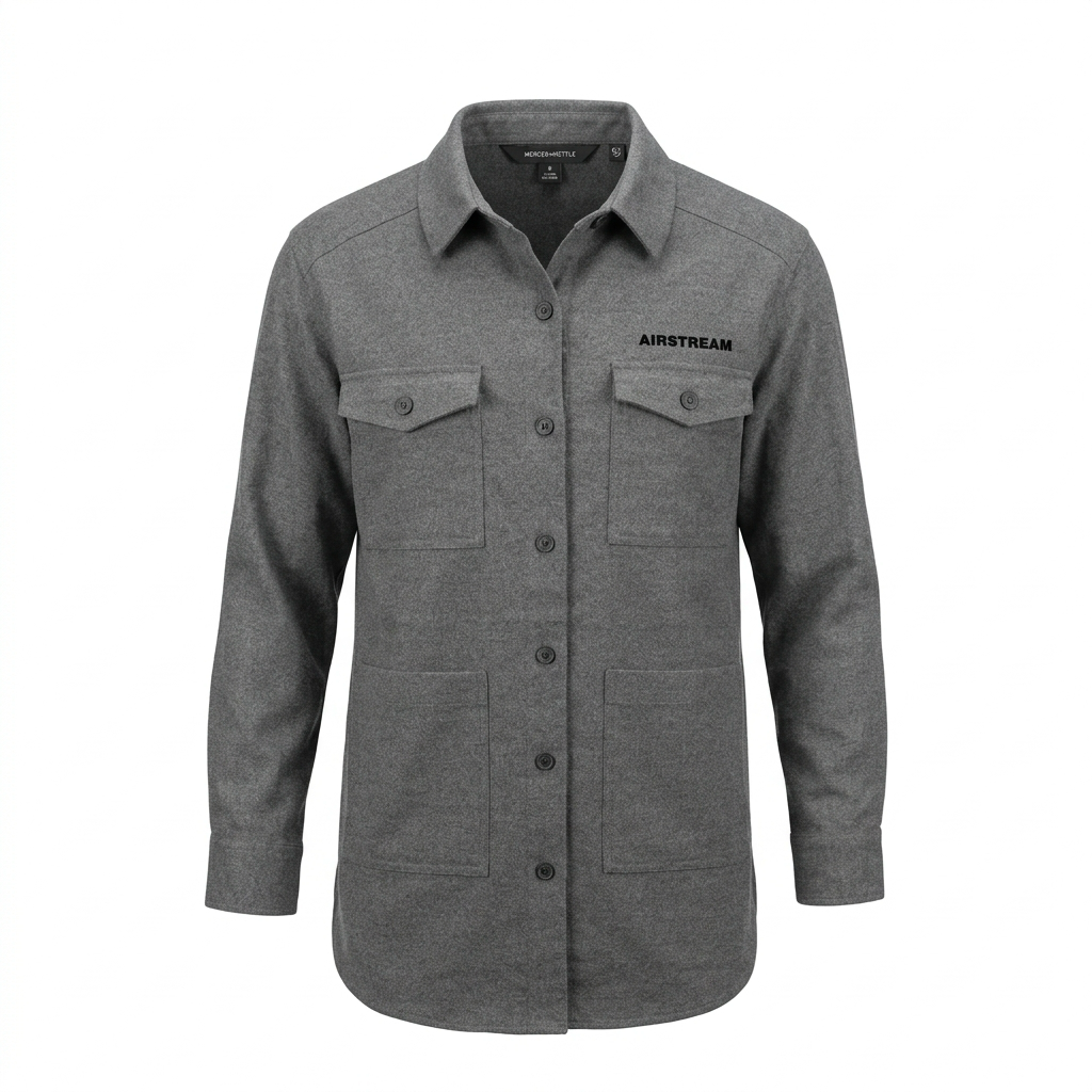 The Airstream Women’s Long Sleeve Twill Overshirt is a gray button-up shirt featuring long sleeves, two chest pockets with flaps, two lower front pockets, and “AIRSTREAM” text on the left chest. Designed as a versatile travel overshirt, it combines style and functionality. The shirt is displayed on a white background.