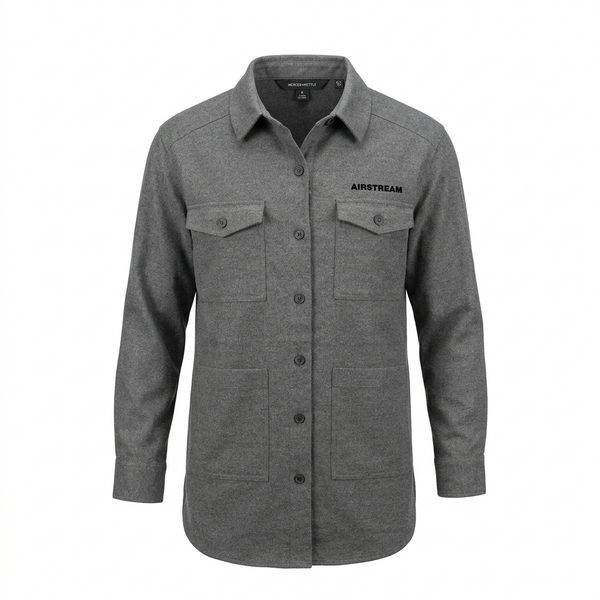 The Airstream Women’s Long Sleeve Twill Overshirt is a gray button-up shirt featuring long sleeves, two chest pockets with flaps, two lower front pockets, and “AIRSTREAM” text on the left chest. Designed as a versatile travel overshirt, it combines style and functionality. The shirt is displayed on a white background.