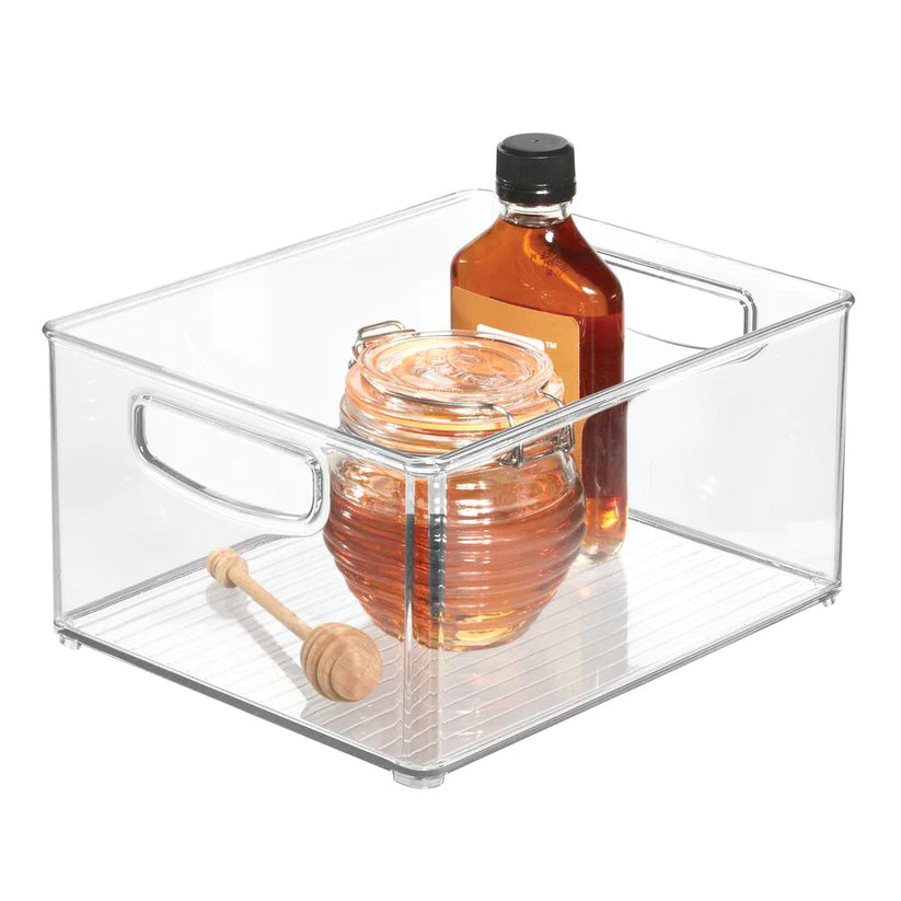 A Recycled Storage Bin, 10 x 8 x 5, made from clear BPA-free plastic and featuring integrated side handles, holds a honey jar with a dipper along with a bottle of syrup. The bin is displayed on a white background.