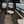 The interior of a camper van or RV showing a spacious seating area with two long dark gray bench seats on either side of a central aisle, a small fold-out wooden table, and windows looking out onto a beach and ocean view.
