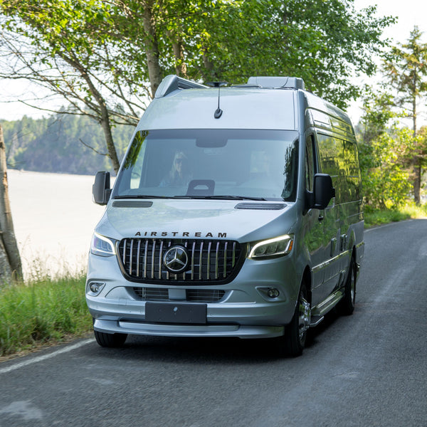 Mercedes-Benz camper van on a road with trees and water in the background
