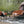 Outdoor camping setup with two tan and black folding camp chairs, a matching folding coffee table, a small side table, and a gray tent in a forest clearing.