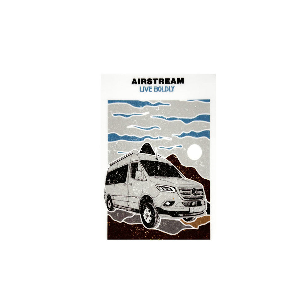 Illustration of the Airstream Touring Coach Live Boldly Sticker, featuring a camper van set against a rocky landscape with mountains, clouds, and either a sun or moon in the background. The design embodies the adventurous spirit of travel sticker art, with “AIRSTREAM LIVE BOLDLY” displayed at the top.