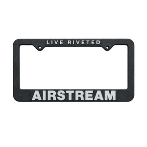 The Airstream Cast Aluminum License Plate Frame, shown here in black with “LIVE RIVETED” displayed at the top and “AIRSTREAM” in bold white letters at the bottom, features a durable cast aluminum construction and a sleek powder coat finish. The frame is photographed against a simple gray background.