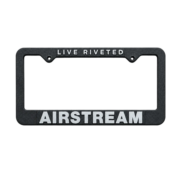The Airstream Cast Aluminum License Plate Frame, shown here in black with “LIVE RIVETED” displayed at the top and “AIRSTREAM” in bold white letters at the bottom, features a durable cast aluminum construction and a sleek powder coat finish. The frame is photographed against a simple gray background.