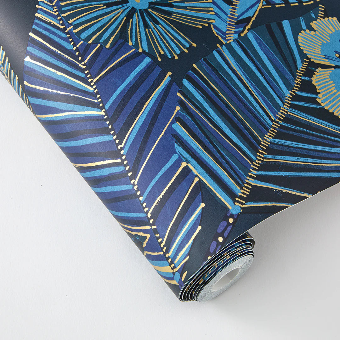A roll of Metallic Bloom Peel + Stick Removable Wallpaper featuring a bold blue and gold tropical leaf and flower pattern is displayed on a white background.
