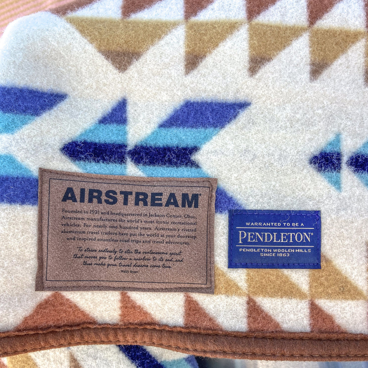 Close-up of the Airstream x Pendleton Woolen Mills Jacquard Blanket, showcasing its brown, blue, and white geometric pattern and stitched-on Airstream and Pendleton brand labels with descriptions.