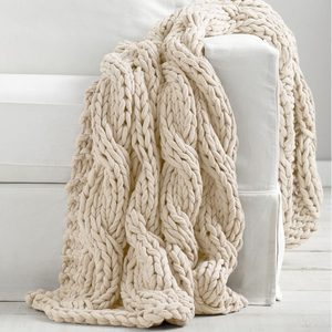Beige chunky knit blanket draped over a white surface