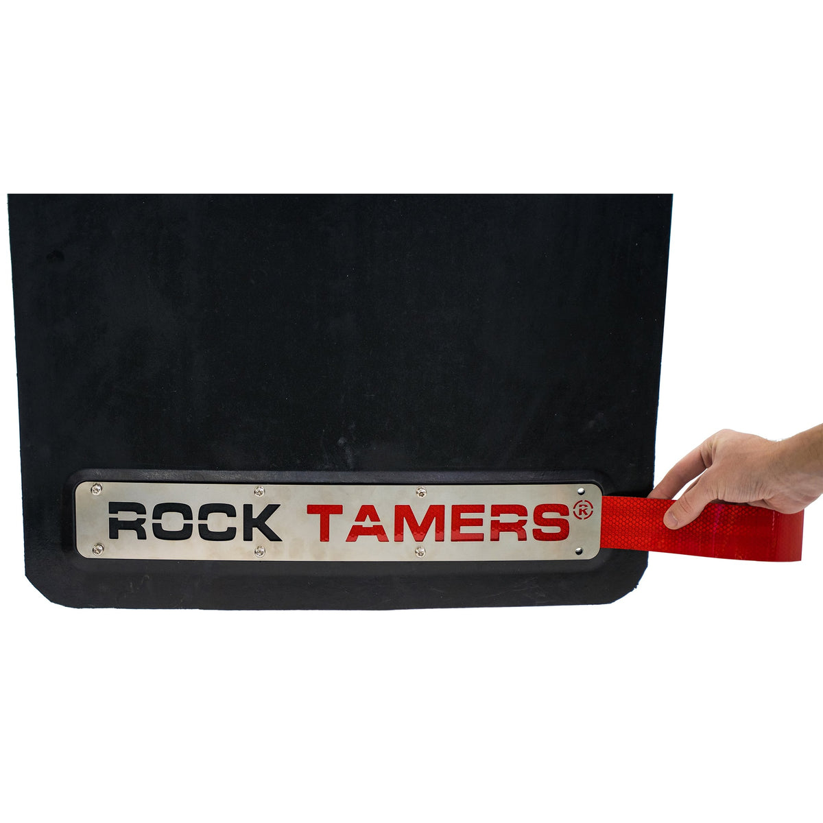 A hand holds a red strap attached to a black mud flap, which features a metal plate and Rock Tamers Red Reflective Tape with durable weatherproof adhesive for extra resilience.
