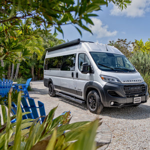 Gray van parked on a gravel road with greenery and blue chairs in the foreground