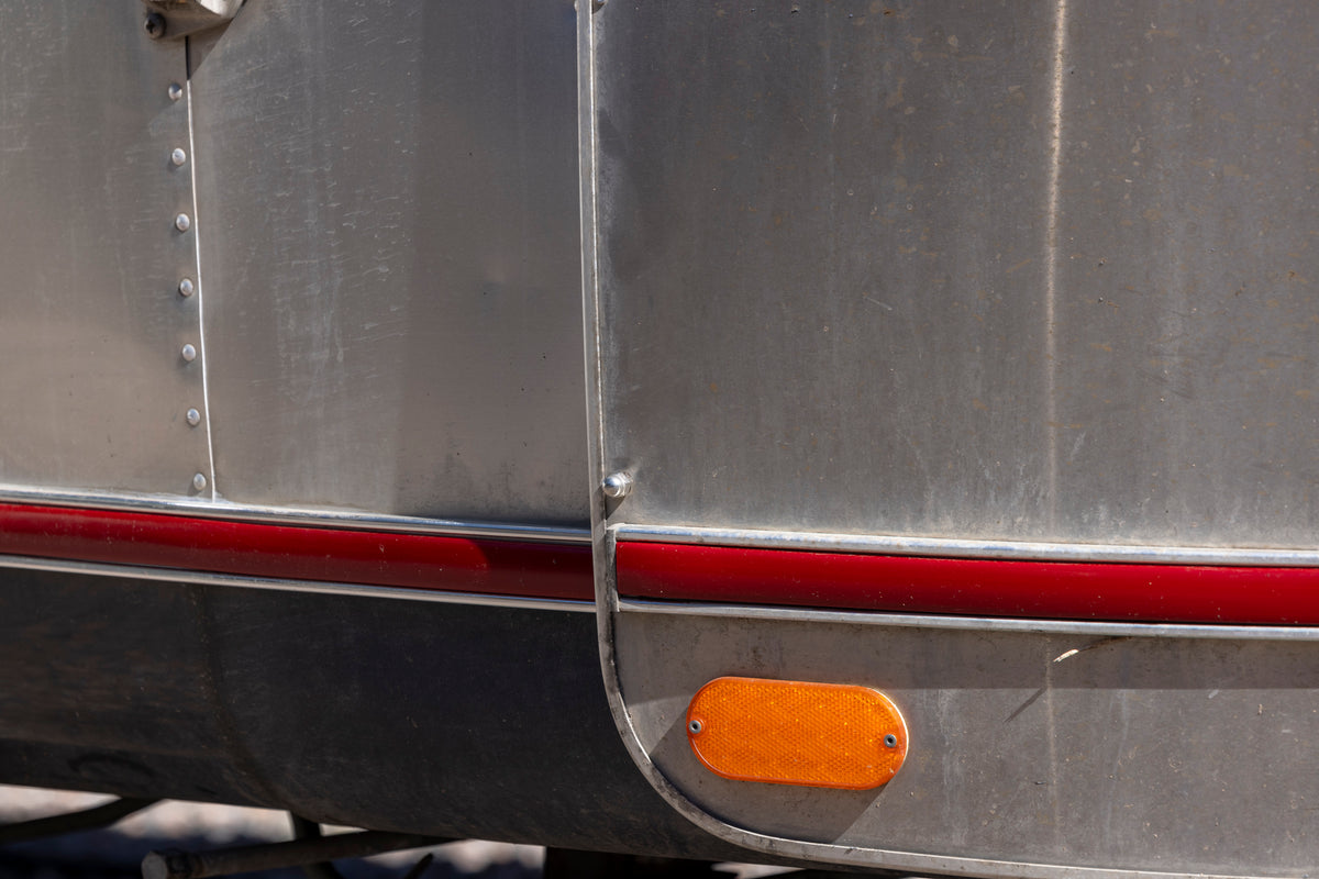 Close-up of a metallic vehicle surface with a red stripe, visible rivets, and an orange reflector near the bottom—highlighting the durability and sleek finish of an Airstream travel trailer equipped with the Airstream Premium Replacement Rub Rail for Travel Trailers.
