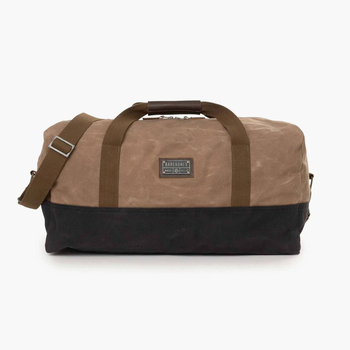 Introducing the Neelum Duffle Bag by Barebones—a stylish two-toned duffel featuring brown canvas on top and black canvas on the bottom, complemented by brown handles and a matching adjustable shoulder strap. Ideal as a weekend or travel bag, it is finished with a classic rectangular patch label sewn on the front for timeless appeal.