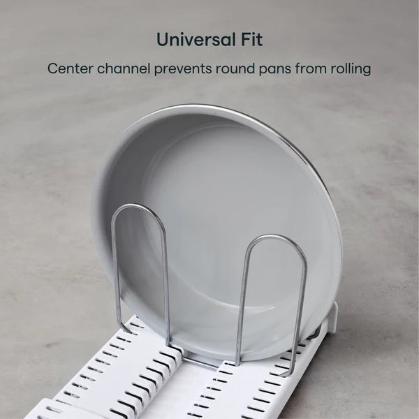 A round white pan is held upright on an Airstream StoreMore Roof Locker Dish Rack by YouCopia with metal dividers. Text above reads: Universal Fit. Center channel prevents round pans from rolling. The rack is placed on a light gray surface.