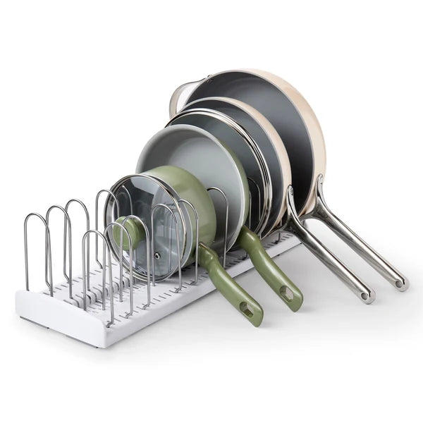 Five frying pans and a glass lid are stacked vertically in a white metal rack with dividers, arranged by size from largest to smallest—a clever solution often found in an adjustable dishware organizer like the Airstream StoreMore Roof Locker Dish Rack by YouCopia.