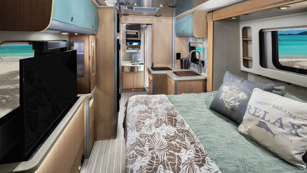 Interior of a modern RV with a bed, kitchen, and entertainment area.
