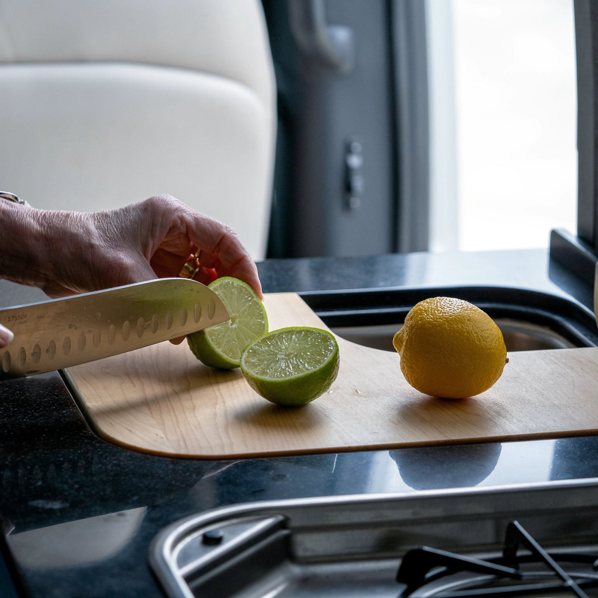 A person slices a lime on an Airstream Custom Sink Cutting Board for Rangeline 21PS/21PL next to a whole lemon in a modern kitchen.