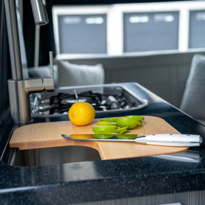 A lemon and sliced lime rest on a wooden cutting board beside a knife atop a kitchen counter, with an Airstream Custom Sink Cutting Board for Atlas 25MS and the sleek design of the Airstream Atlas 25MS visible in the background.