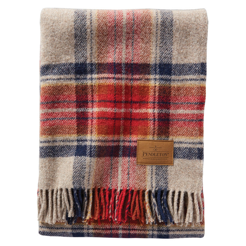 A folded Motor Robe Throw with Leather Carrier by Pendleton, crafted from wool and featuring a classic plaid pattern in red, navy, and beige tones. The travel blanket includes fringe detailing on one end and displays a brown Pendleton label sewn on the front.