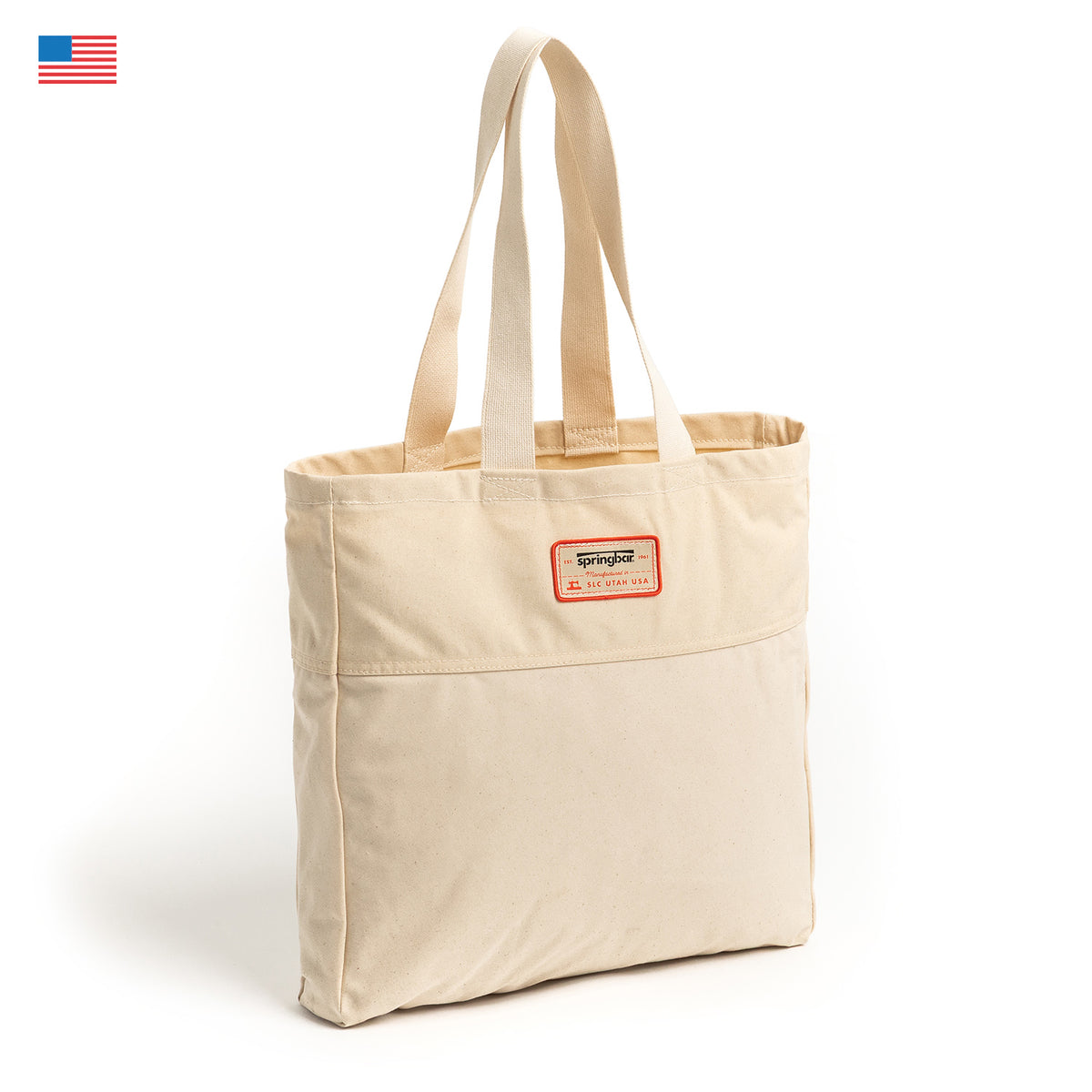 A beige Camp Tote by Springbar made from Sunforger Cotton Duck Canvas, featuring two handles, a front pocket, and a small red “Springer” label on the front. The classic Springbar-inspired design is showcased against a white background with a small US flag in the top left corner.