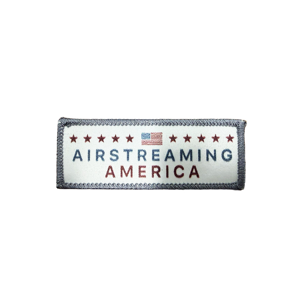 Introducing the Airstreaming America Heat Applied Printed Patch—a rectangular iron-on patch showcasing bold red stars, a small American flag, and “Airstreaming America” written in striking blue and red lettering on a crisp white background. This heat-applied patch is the perfect way to add classic Americana flair to your favorite gear.