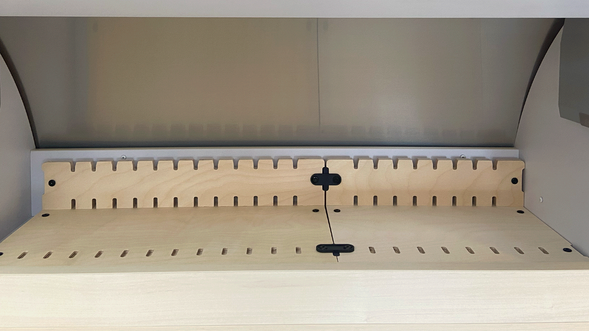 A close-up of the Airstream Roof Locker Organization by Airworthy Equipment Company, showing a wooden shelf with evenly spaced vertical slots and two black fasteners securing the panels together inside an overhead storage organizer within a cabinet or storage unit.