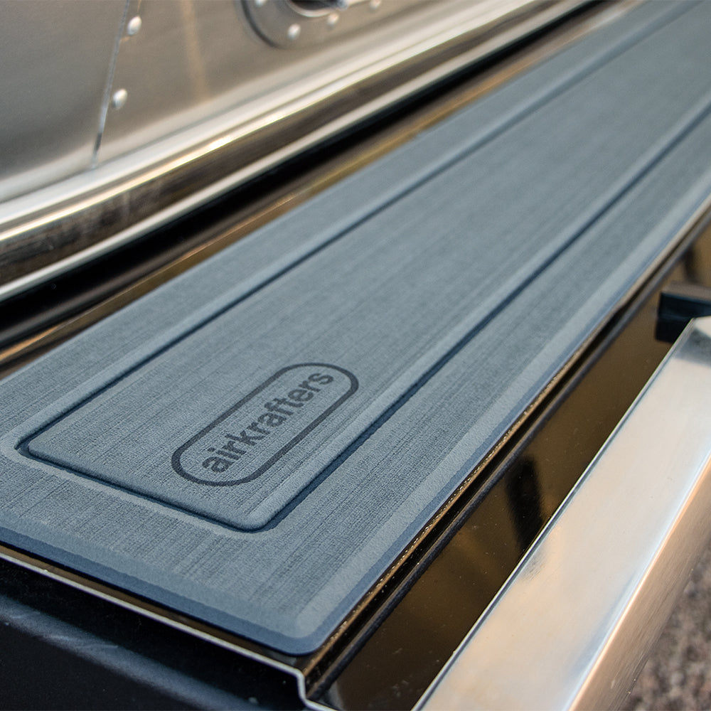 Close-up of a grey bumpMAT™ by Airkrafters with “airstream” embossed on it, placed on a shiny metal surface—likely the step or bumper of a vehicle. This protective mat is an essential travel trailer accessory, delivering both style and functionality.