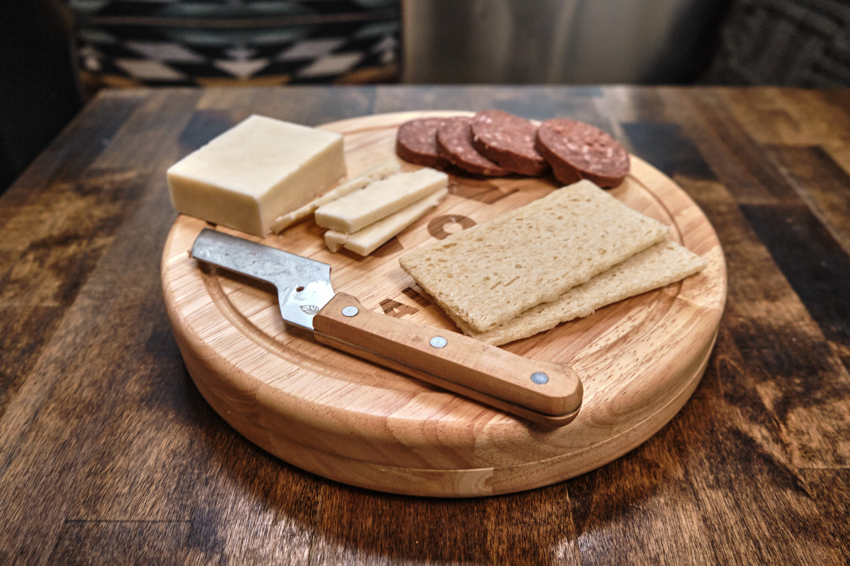 The Airstream Bamboo Cheese Cutting Board Set, featuring slices of cheese, sausage, and bread alongside a cheese knife with a wooden handle, is elegantly arranged on a rustic brown table—perfect for any gathering or as a standout piece in your favorite cheese board collection.
