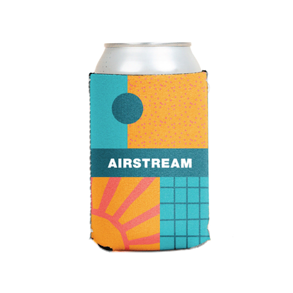 A stylish neoprene can cooler called the Airstream Colorblock Live Riveted Can Cooler features a colorful sleeve with geometric patterns—including a sun, grid, circle, and orange and teal shapes—and displays the word “AIRSTREAM” in bold white letters across the middle.