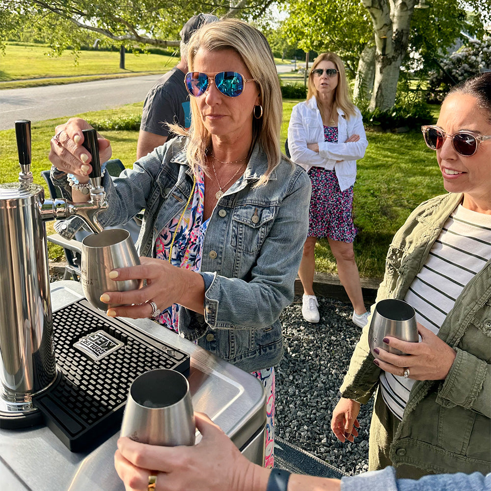 People at an outdoor event with a bar setup and people in the background.