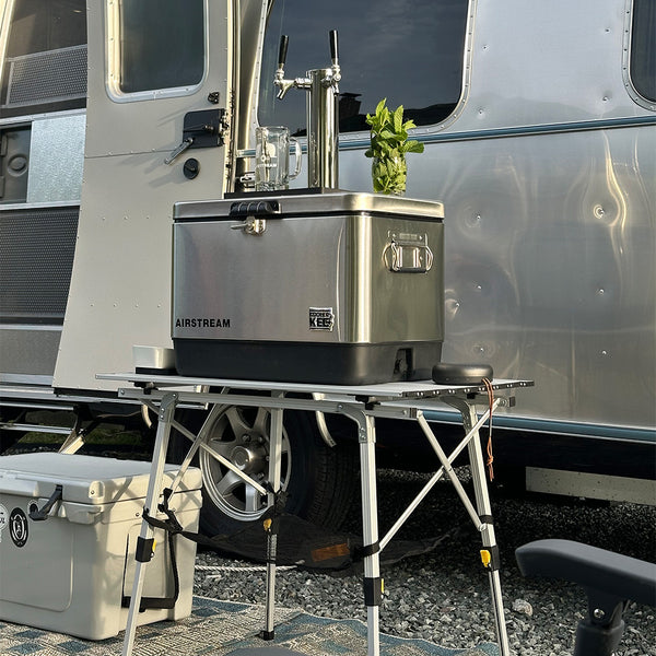 Outdoor kitchen setup with Airstream cooler and table in front of a trailer