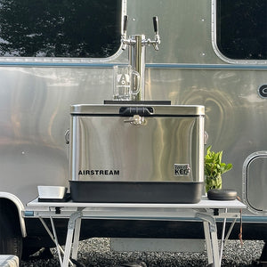 Stainless steel cooler with Airstream branding in front of a camper trailer.