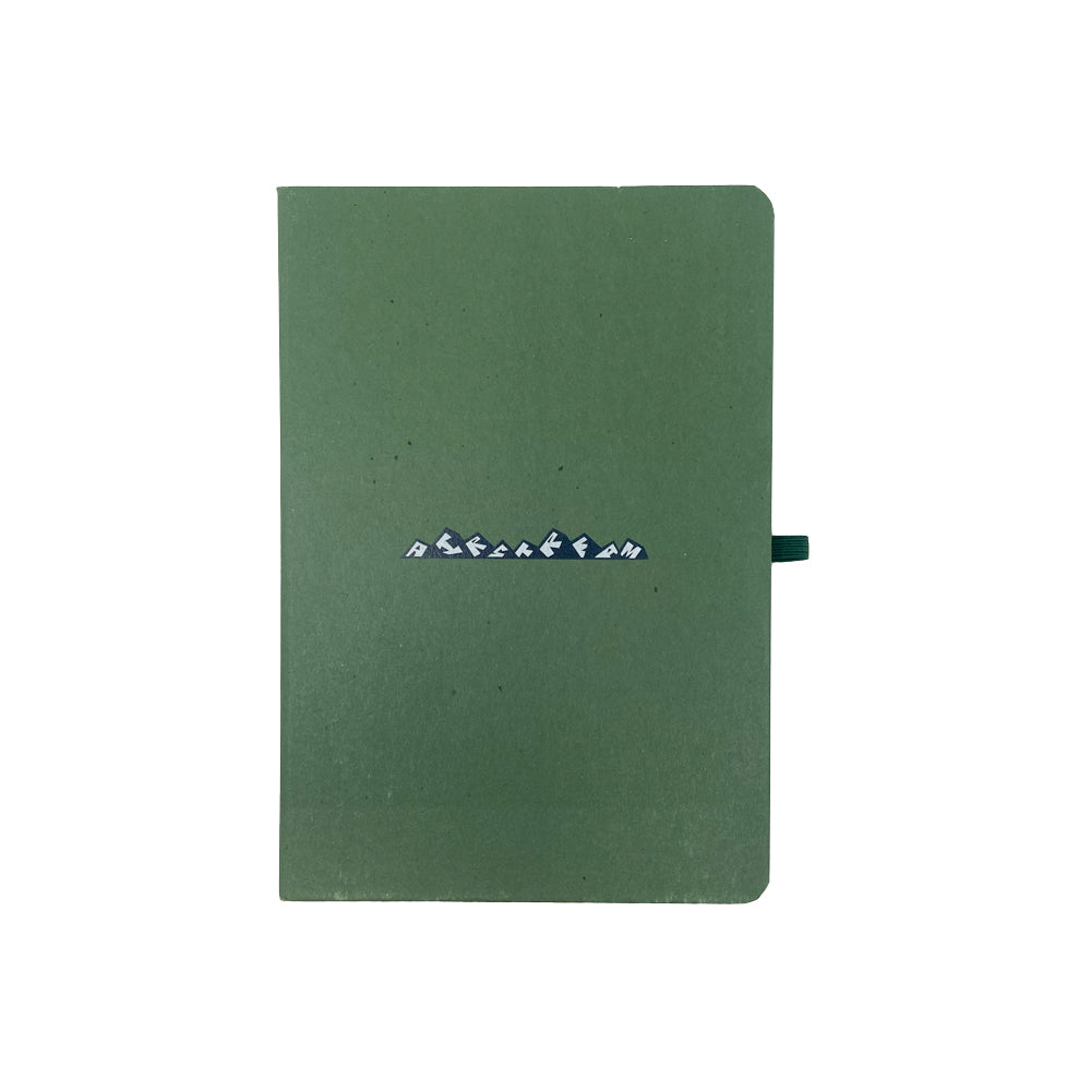A green Airstream Mountains Distressed Journal featuring a pen loop on the right side and small stylized white text across the center of the cover, set against a plain white background.