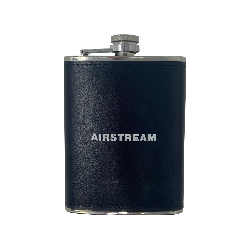 The Airstream Flask is an elegant 8oz black flask, wrapped in leather with a silver cap and the word “AIRSTREAM” printed in white on the front, displayed against a clean white background.