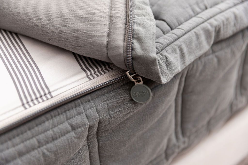 Close-up of the Airstream RV Fit Beddy’s for Flying Cloud Travel Trailers in gray, featuring a partially open zipper that reveals a striped bedsheet beneath—perfect for zippered bedding enthusiasts. The zipper pull displays a round bedxS by gravity tag, making it an ideal choice for RV mattress or Airstream bedding setups.
