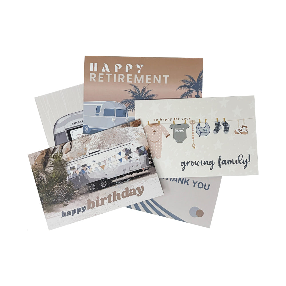 A set of four Airstream Assorted Occasion Cards, overlapping to show diverse designs: messages include “Happy Retirement,” “growing family!” (with baby clothes imagery), “happy birthday,” and a partial “THANK YOU.” This assorted pack features festive Airstream RVs, palm trees, and lively decorations—ideal for celebrating all of life’s special occasions.