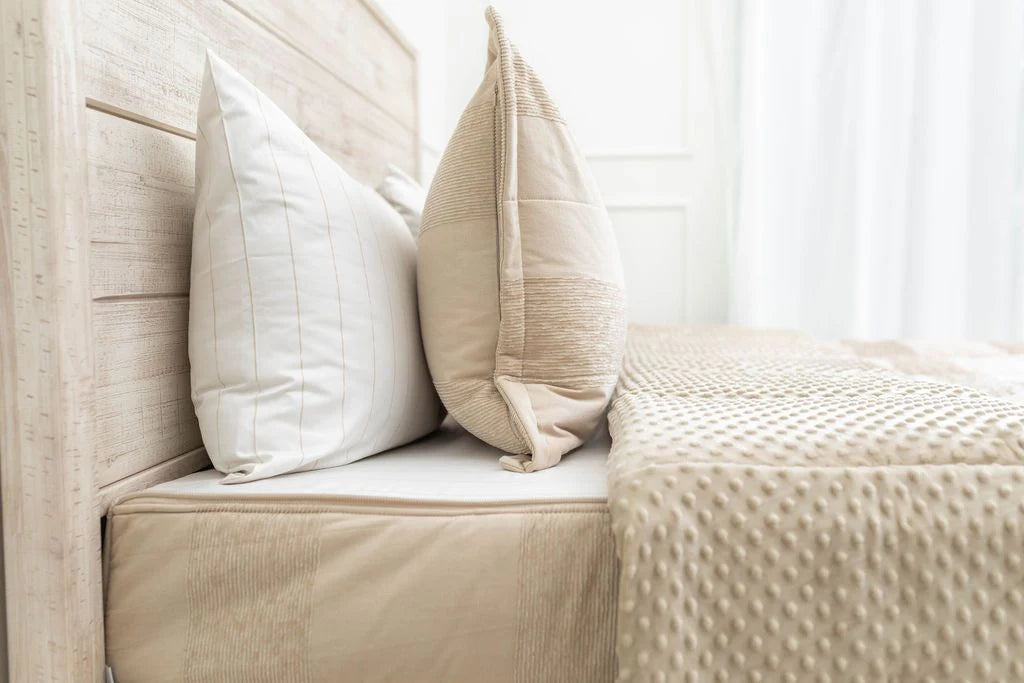 Close-up of a neatly made bed with beige and white pillows, a soft textured beige blanket, and a light wooden headboard, featuring the Airstream RV Fit Beddy’s for Excella Travel Trailers—stylish bedding designed specifically for RV living.