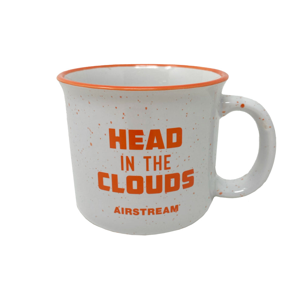 The Airstream Head in the Clouds Mug is a white ceramic mug adorned with orange speckles and an orange rim, featuring bold orange text that reads “HEAD IN THE CLOUDS” with “AIRSTREAM” underneath—making it the perfect Airstream mug for travel enthusiasts.