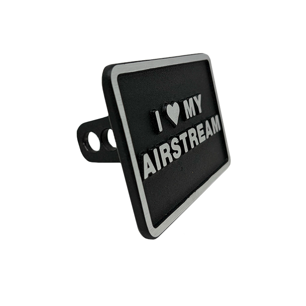 A black, rectangular Airstream 2″ Hitch Cover with a powder-coated finish and raised white text reading “I ♥ MY AIRSTREAM,” shown from an angled perspective.