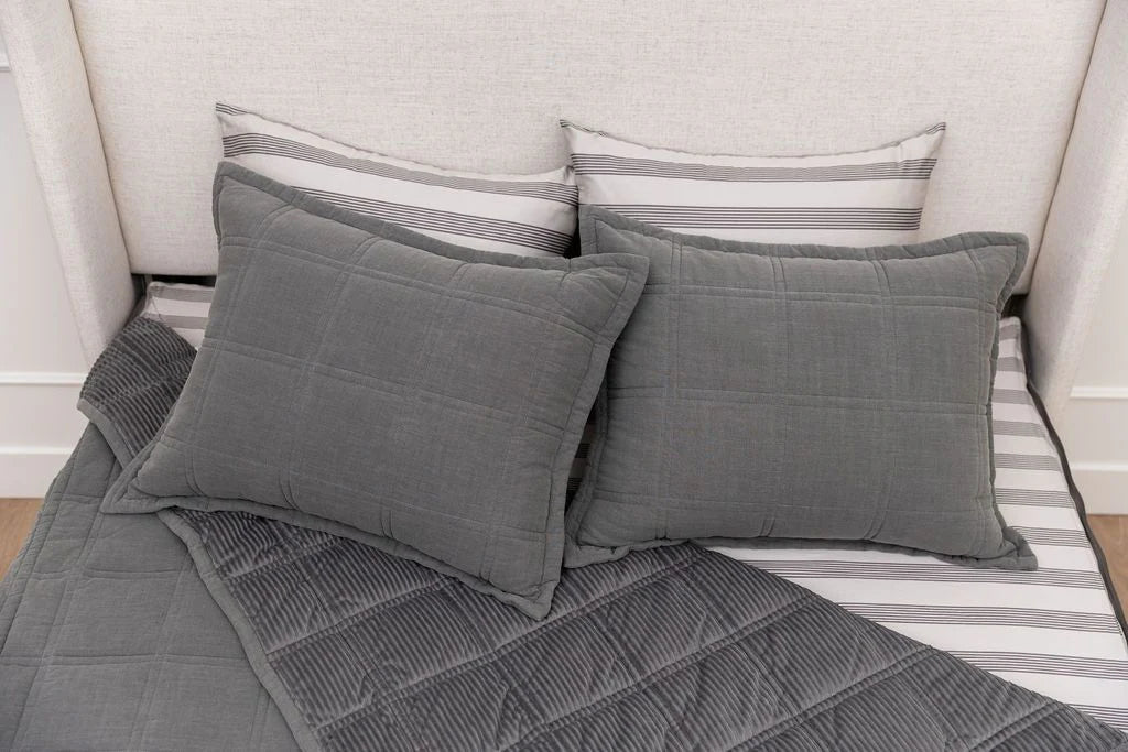 Two gray quilted pillows and a matching blanket from the Airstream RV Fit Beddy’s for Flying Cloud Travel Trailers are arranged on a neatly made bed with white and gray striped pillowcases and sheets. The light-colored upholstered headboard adds to the cozy setting, making it an ideal choice for stylish bedding in any Airstream or RV mattress setup.
