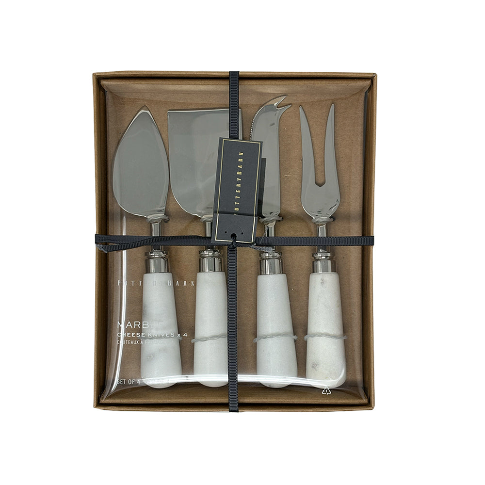 The Airstream x Pottery Barn Cheese Knife Set features four cheese knives with elegant white marble handles and silver blades, artfully arranged and tied with a black ribbon inside a brown gift box.