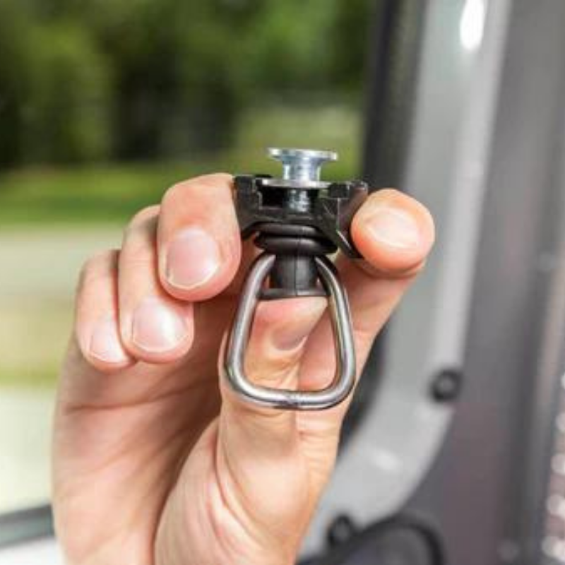 A hand holds a Quick-Release Latch for Interstate 24X, 19X, and REI Co-op Special Edition Basecamp—featuring a D-ring and threaded bolt—designed for securing cargo or attaching equipment to the L-Track Storage System inside an Airstream.