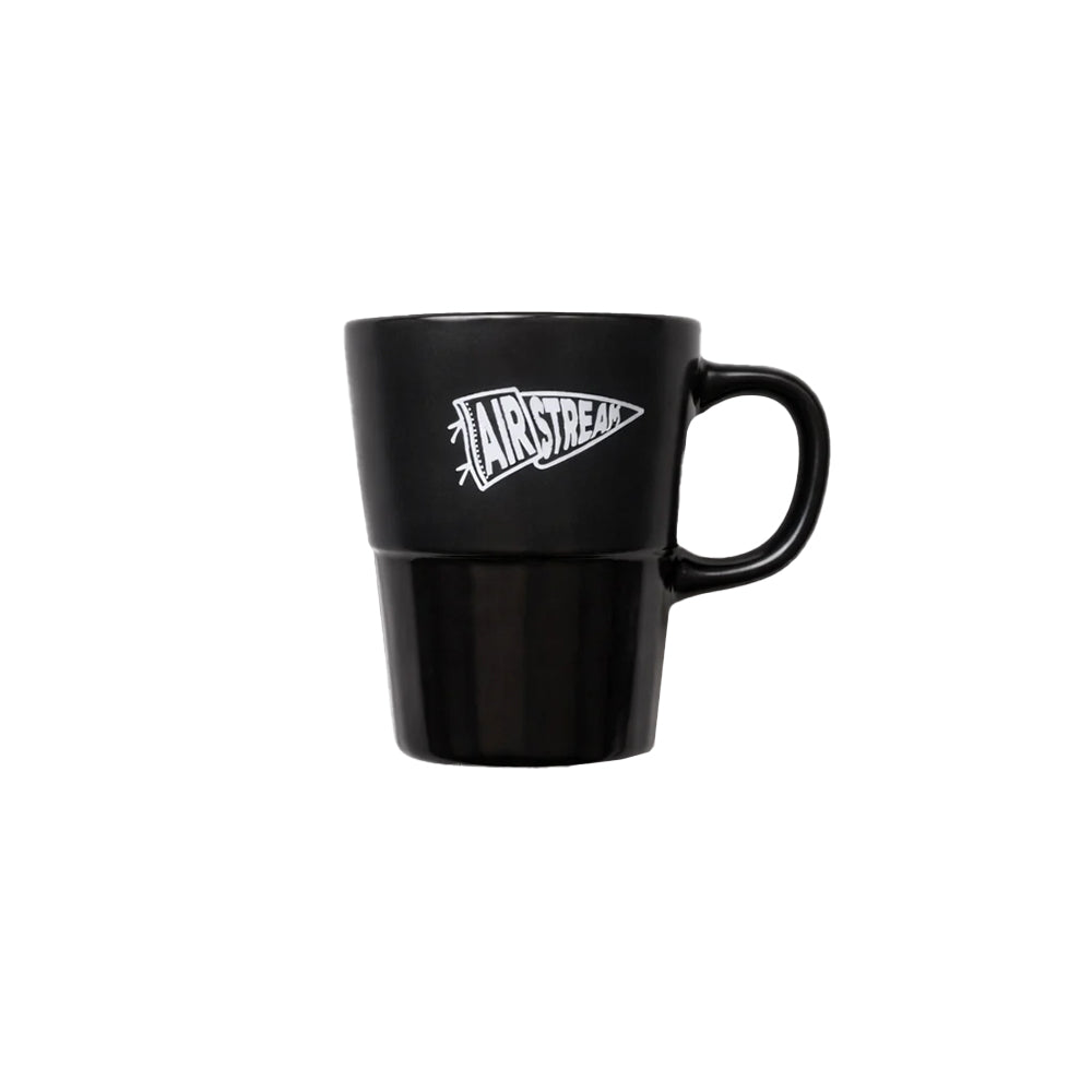 The Airstream Rally Pennant Mug is a black ceramic mug with a handle, displaying a bold white graphic that reads “AIRSTREAM” in a stylized font—perfect for Airstream enthusiasts or anyone looking for a unique gift.
