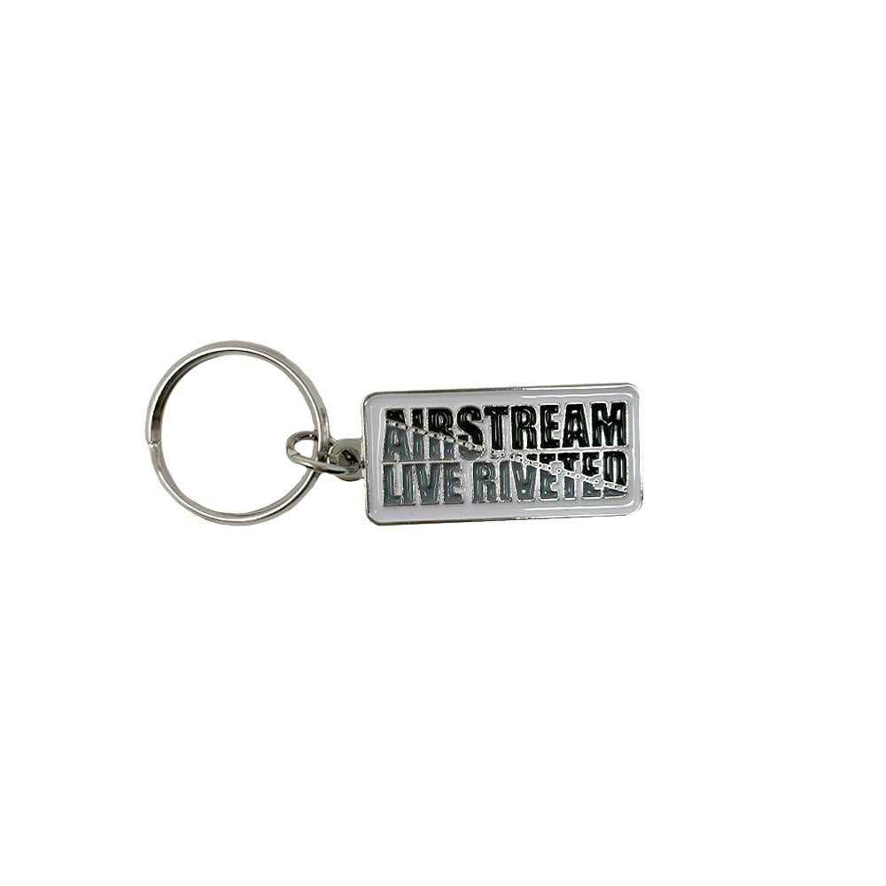 Introducing the Airstream Rivet Line Metal Keychain—a sleek, rectangular silver accessory featuring raised black text that proudly reads “AIRSTREAM LIVE RIVETED.” Perfect for any Airstream enthusiast, this durable metal keychain is securely attached to a standard metal key ring.