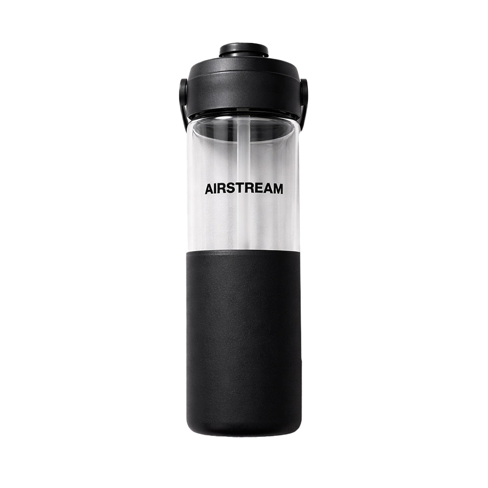 The Airstream Glass Silicone Sleeve Water Bottle is shown against a white background, featuring clear glass construction with a black lid, a black silicone sleeve covering the lower half, AIRSTREAM printed in bold black text, and a convenient straw.