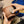 A person holds a handmade terracotta clay mug with a carved 'STOCKTON' logo on the side. The mug is shown in a close-up, lifestyle setting with hands holding it and a blue bag in the background.