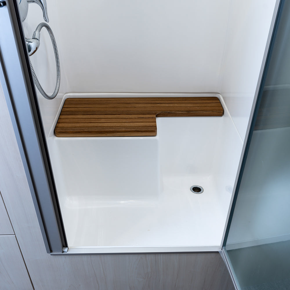 Shower with a white base, an Airstream Teak Shower Bench for Bambi Travel Trailers featuring a cut-out section for added comfort, a floor drain, a sliding glass door, and a wall-mounted handheld shower head—perfect for those seeking stylish custom Airstream accessories.