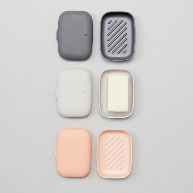 Two rectangular Bamboo Travel Soap Boxes by Ekobo, in gray and cream, are shown open with their matching lids beside them. The cream box holds a bar of soap while the gray one is empty. These eco-friendly containers are designed to be leak-proof for mess-free transport, keeping your bar soap clean and secure wherever you go.