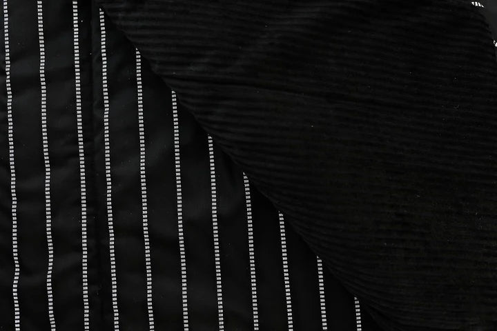 The Bryant Luxe Blanket by Beddy’s, featuring a modern black fabric with white vertical dashed lines, is partially covered by another piece of textured black fabric laid diagonally across the top right corner.